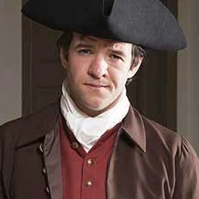 Man in historical 18th-century attire with a tricorn hat and dark coat.