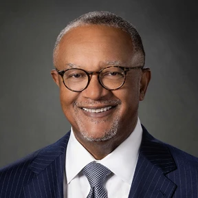 Portrait of a man wearing glasses and a dark blue pin-striped suit.